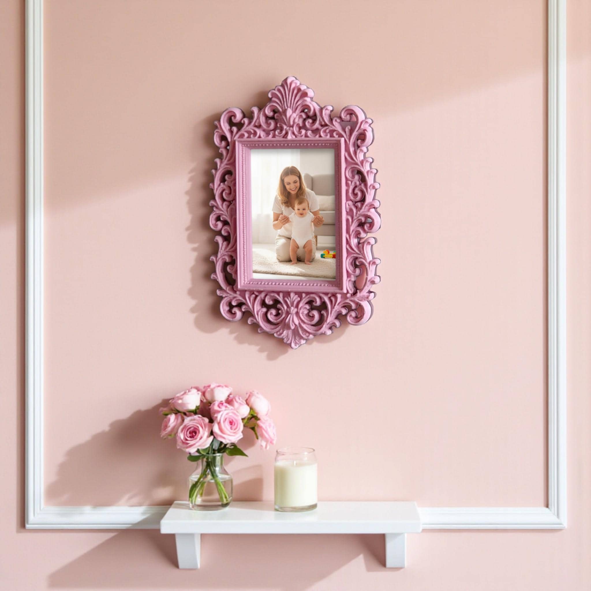 May include: A decorative pink picture frame with an elaborate, swirling design. The frame contains a photograph of a woman and child in a park. The frame is on a white shelf, with pink flowers and a candle.