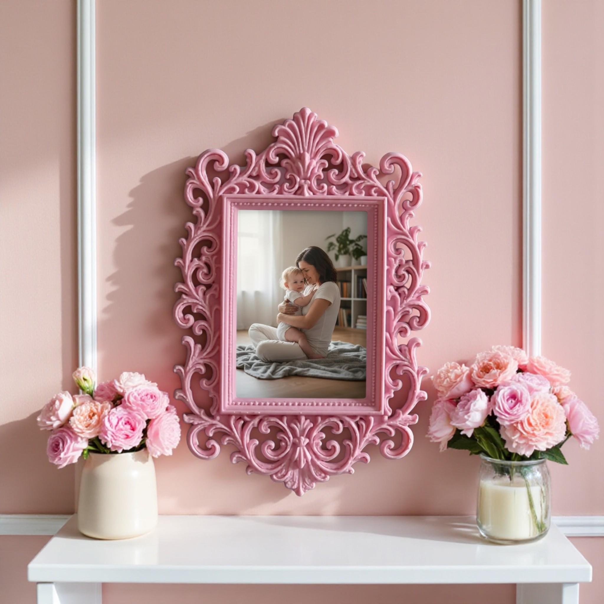May include: A decorative pink picture frame with an elaborate, swirling design. The frame contains a photograph of a woman and child in a park. The frame is on a white shelf, with pink flowers and a candle.