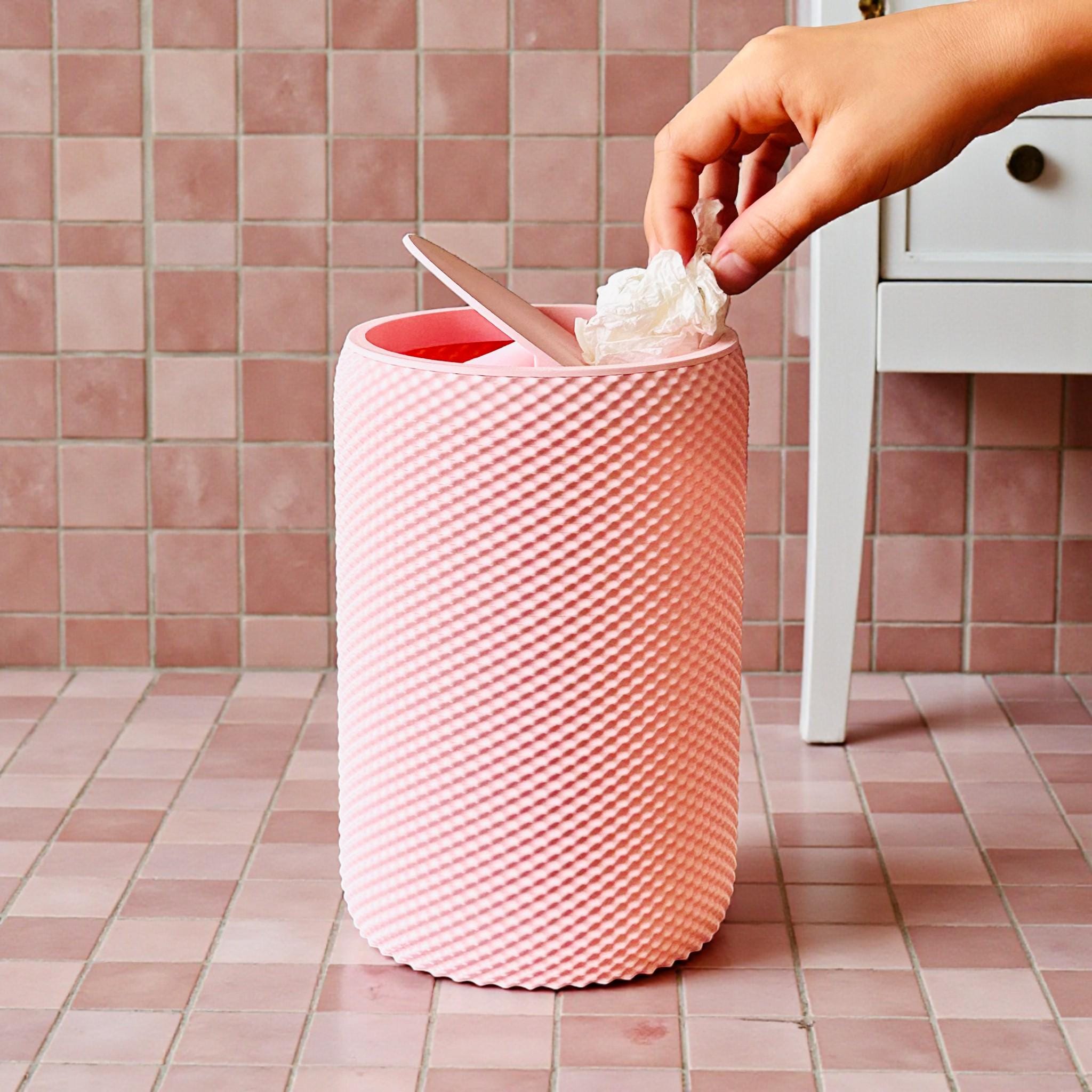 Pink textured trash can with a hand disposing of trash against a tiled wall.