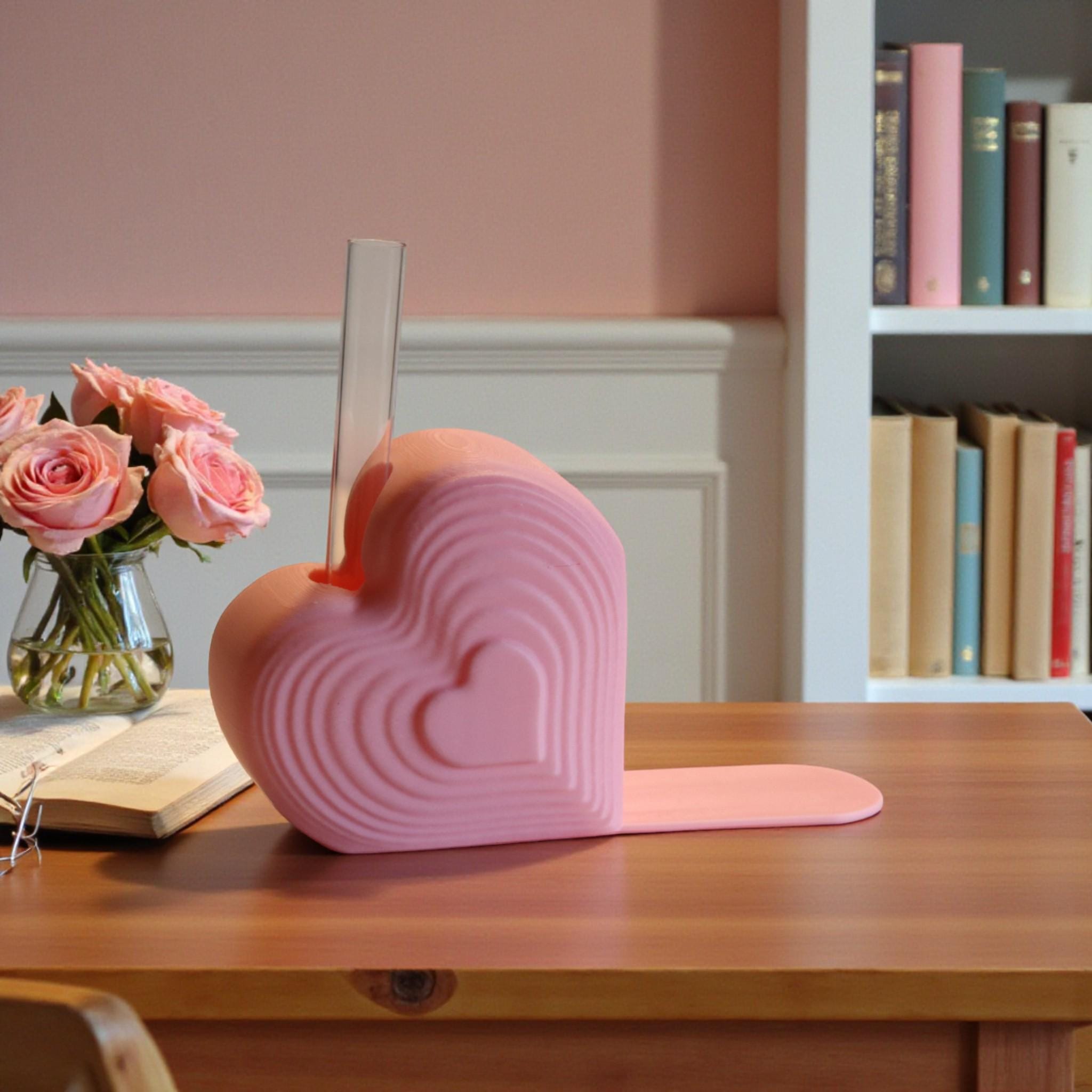 Pink heart bookend that doubles as a test tube vase, styled on a desk with books; romantic shelf decor and Valentine’s gift for book lovers.