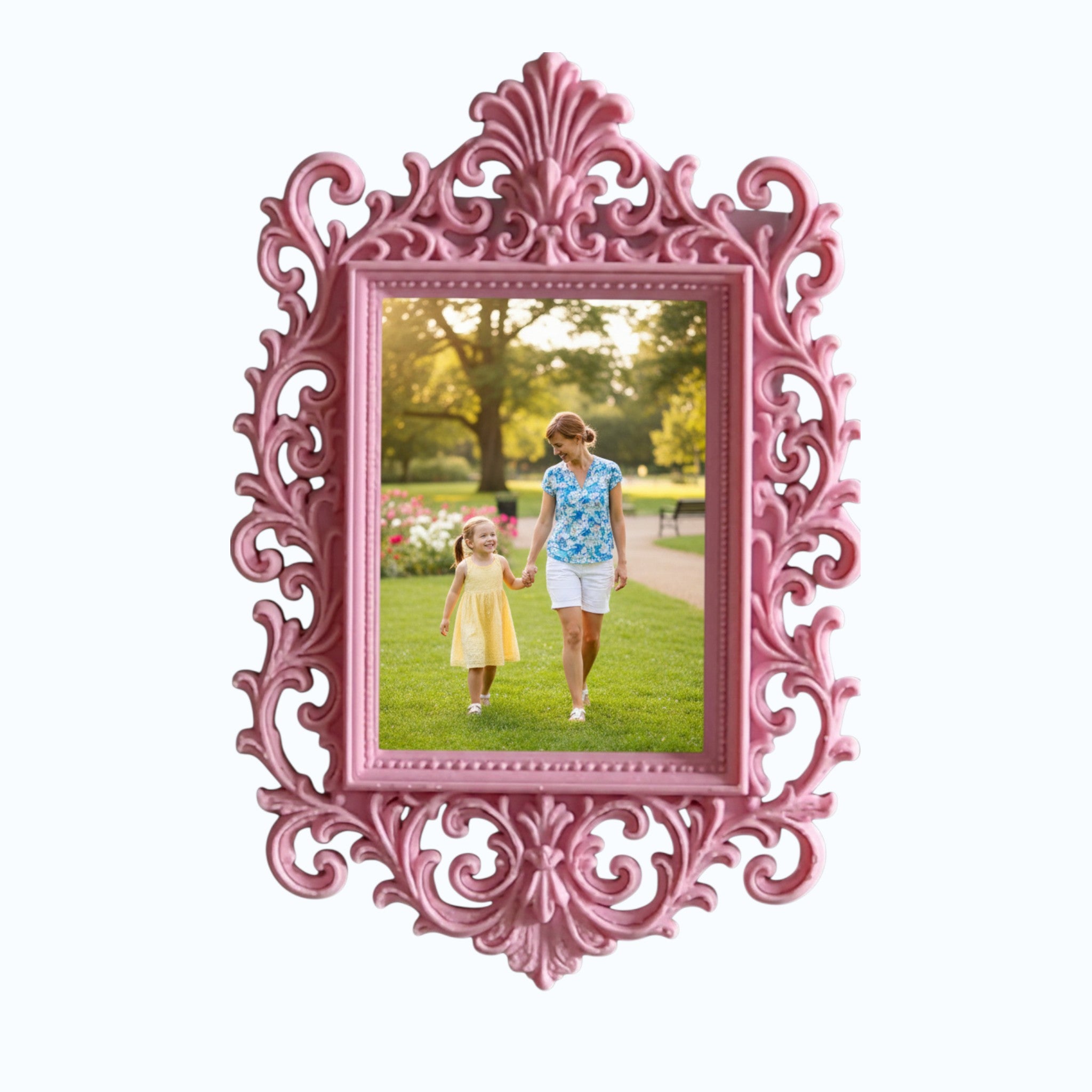 May include: A decorative pink picture frame with an elaborate, swirling design. The frame contains a photograph of a woman and child in a park. The frame is on a white shelf, with pink flowers and a candle.