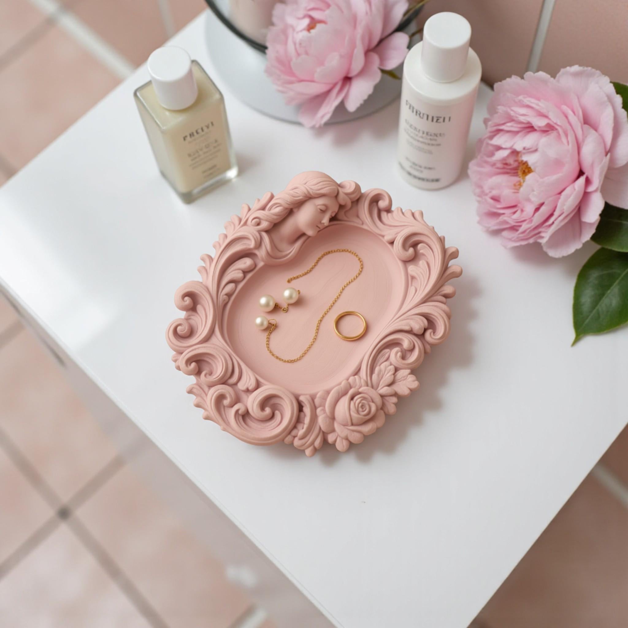 Pink rococo-style woman and rose catchall tray used as a jewelry dish, holding a gold ring, pearl earrings, and a necklace on a vanity surface.