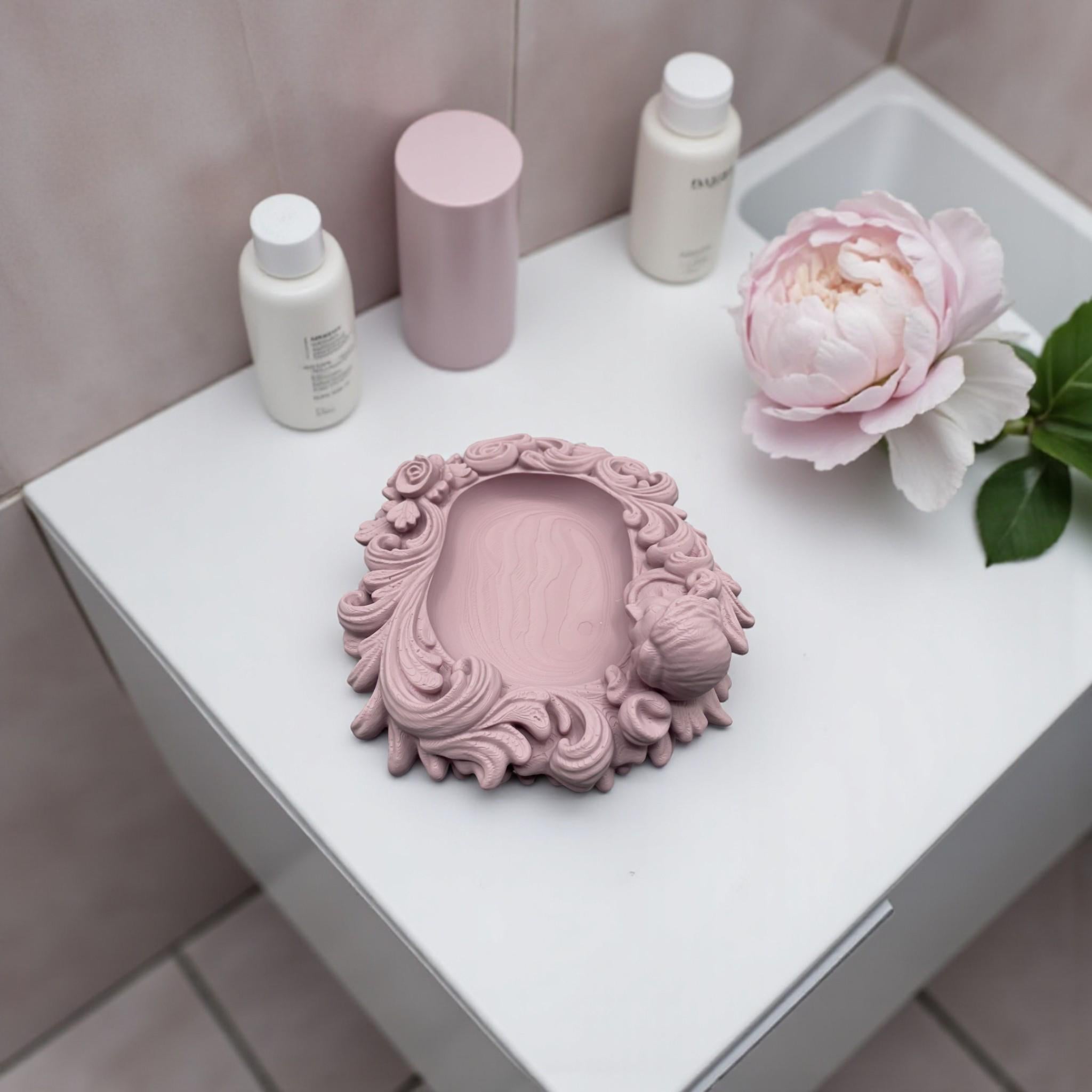 Pink rococo-style woman and rose catchall tray used as a jewelry dish, holding a gold ring, pearl earrings, and a necklace on a vanity surface.